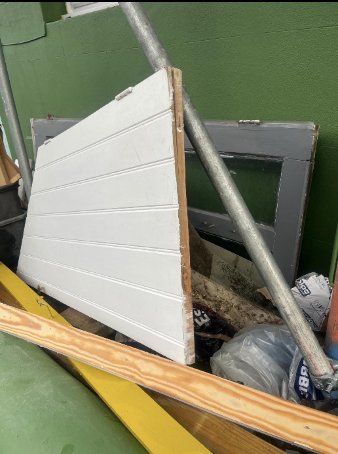 Old doors, frames and building materials stacked against a green wall.