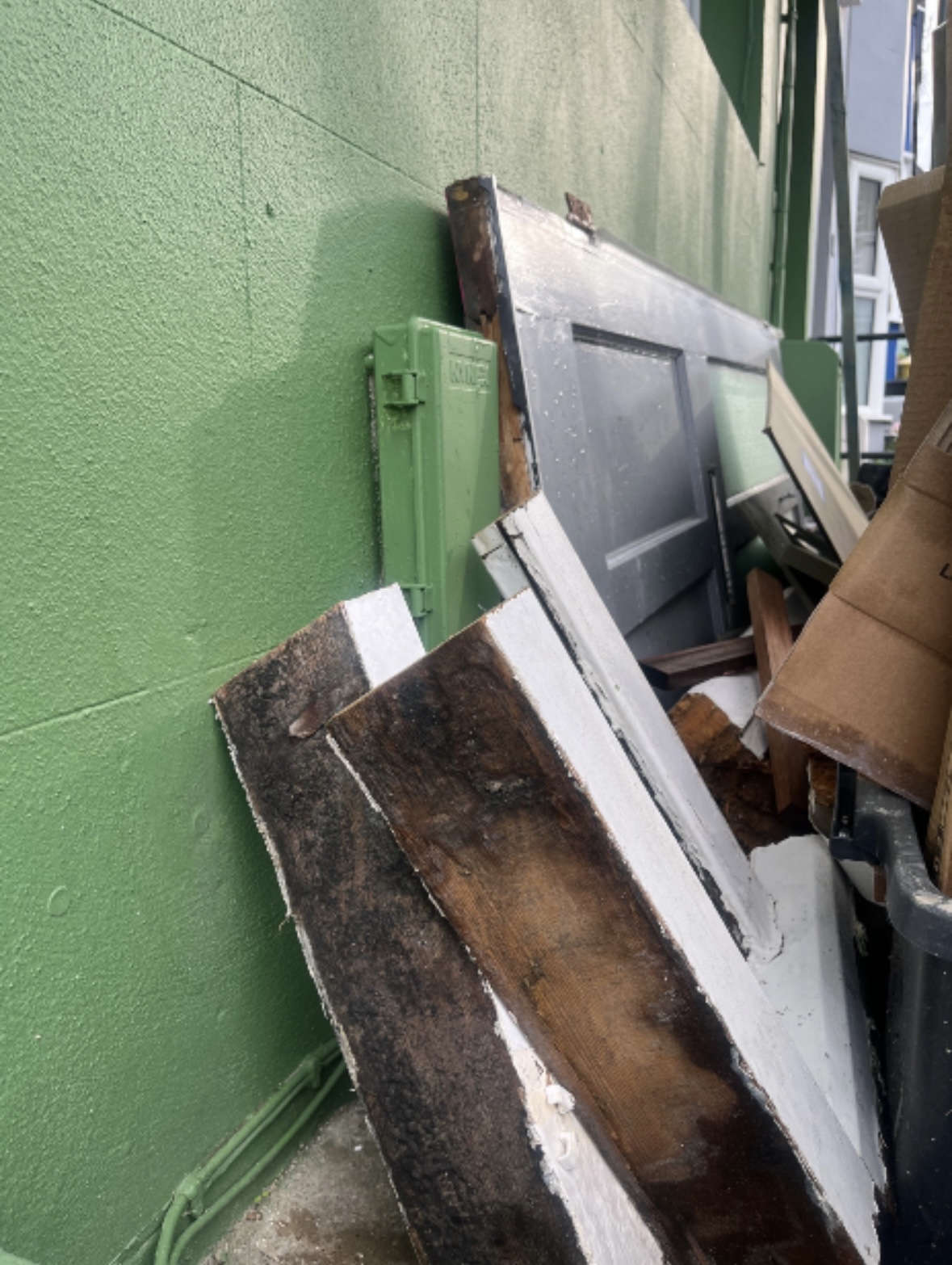 Old timber sections and doors stacked neatly against a wall ready for collection.