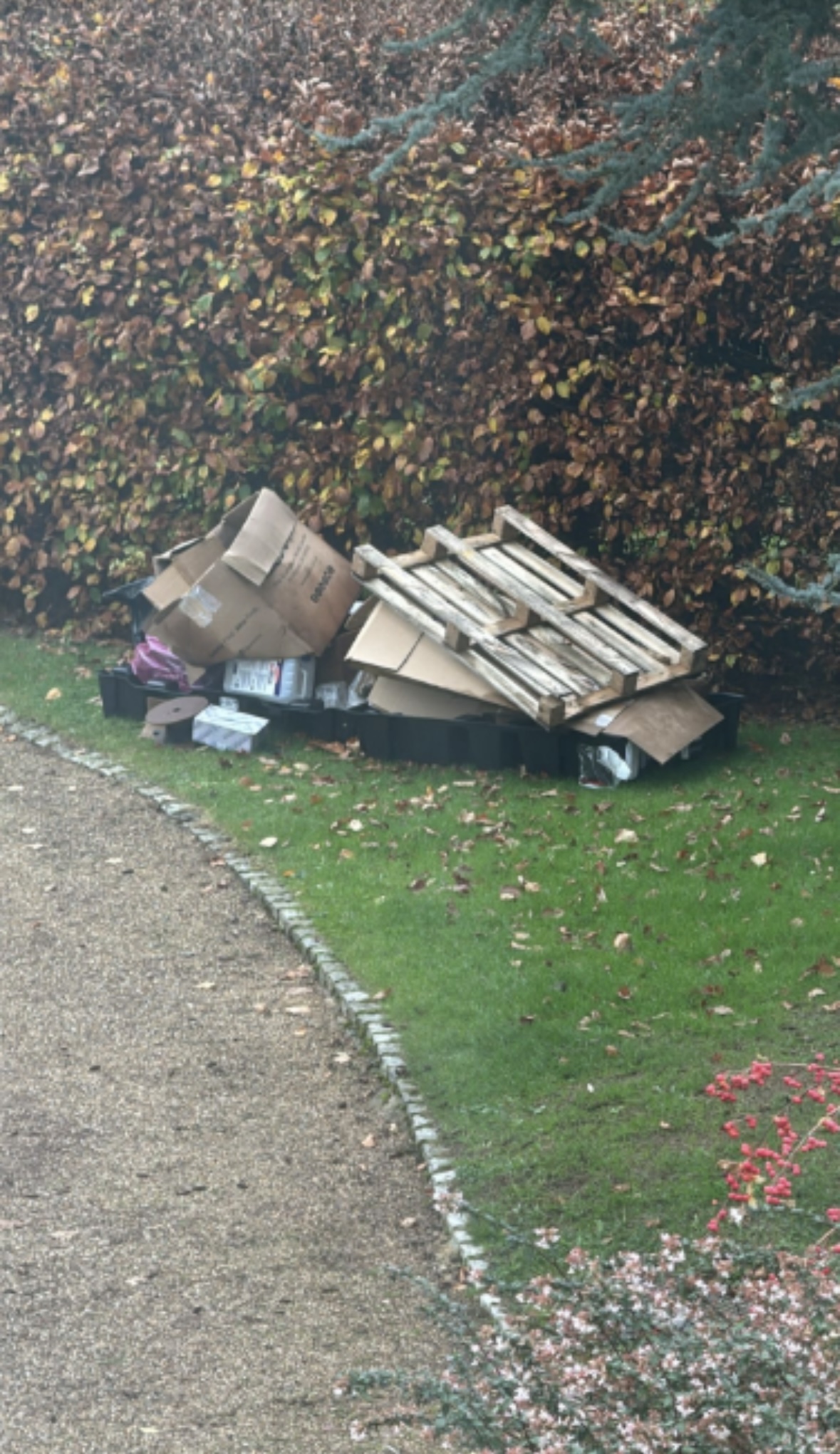 Pallets and cardboard piled neatly beside a hedge in a large garden.